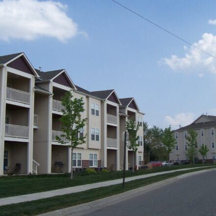 Apartment buildings lining a quiet residential street under a blue sky.