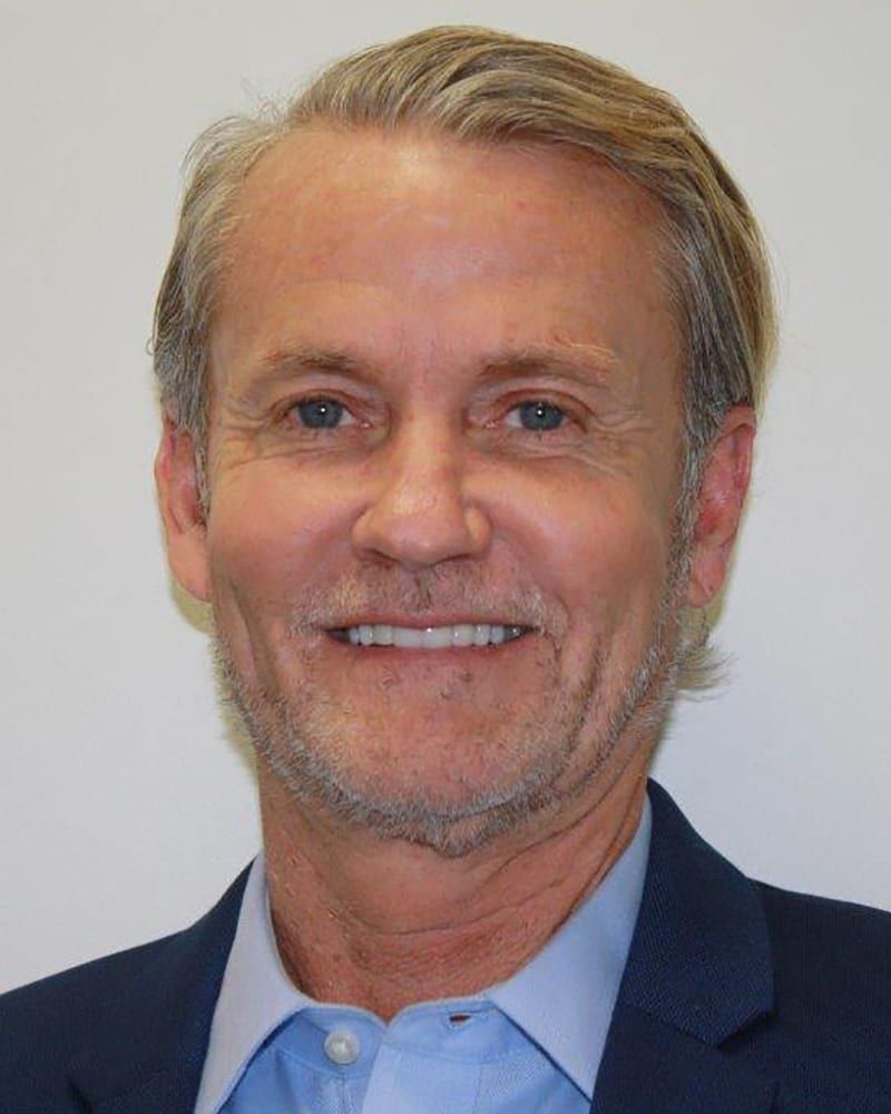 Portrait of a smiling man in a dark blazer and light blue shirt against a plain background