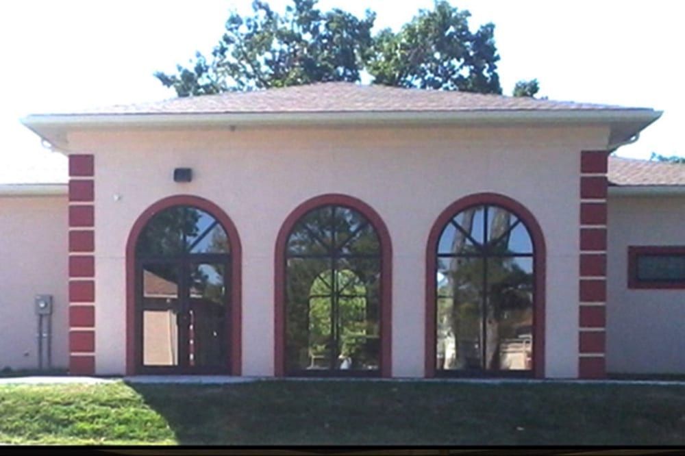 Front view of a beige building with three arched windows and red brick accents