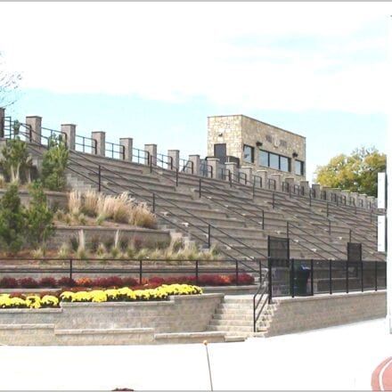 Outdoor amphitheater with stone seating, flowers, and a staircase under a bright sky