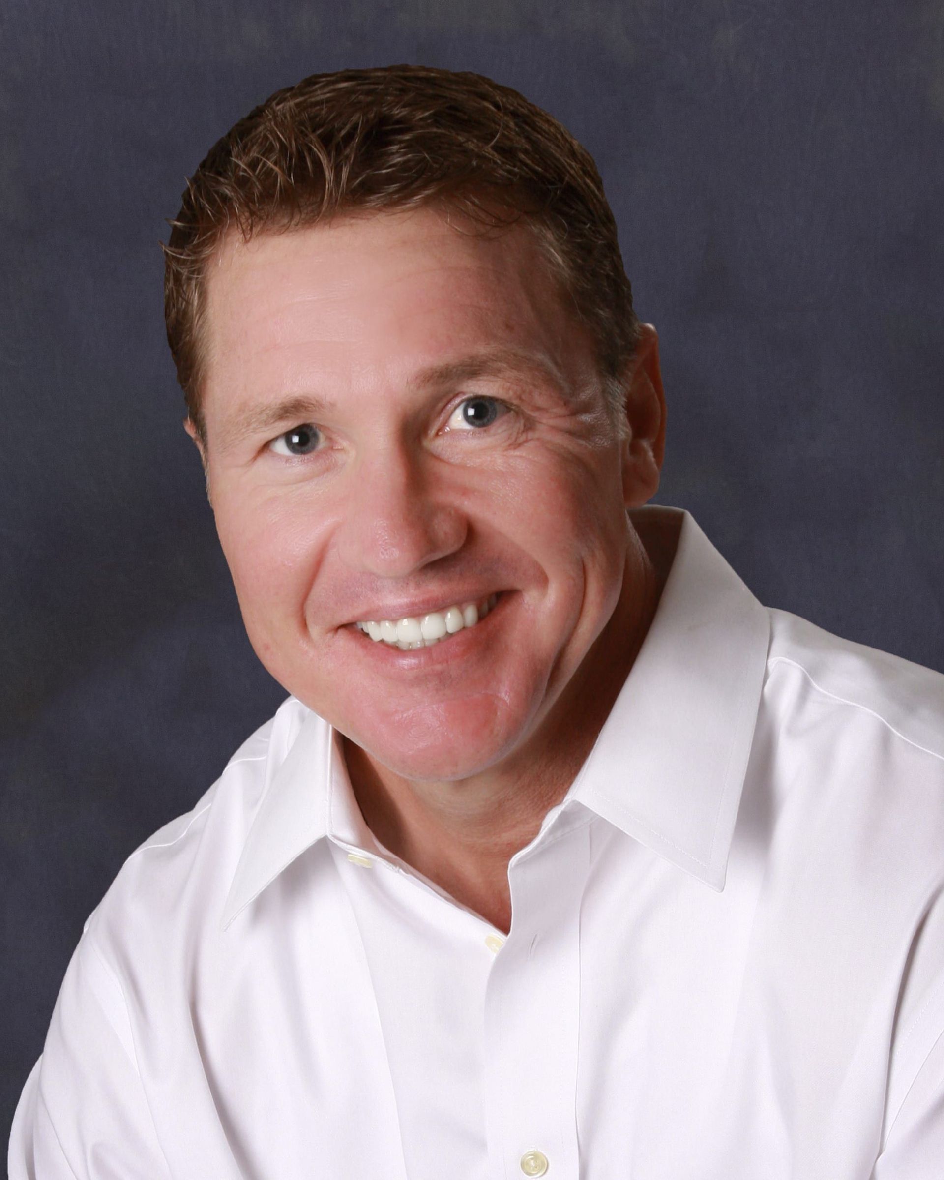 Smiling person in a white shirt against a dark studio background