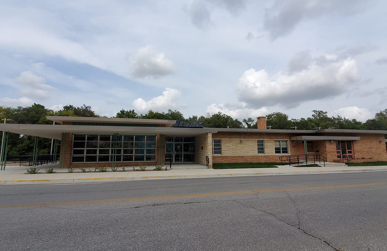 Single-story brick building with glass entrance under cloudy sky, seen across a parking lot.
