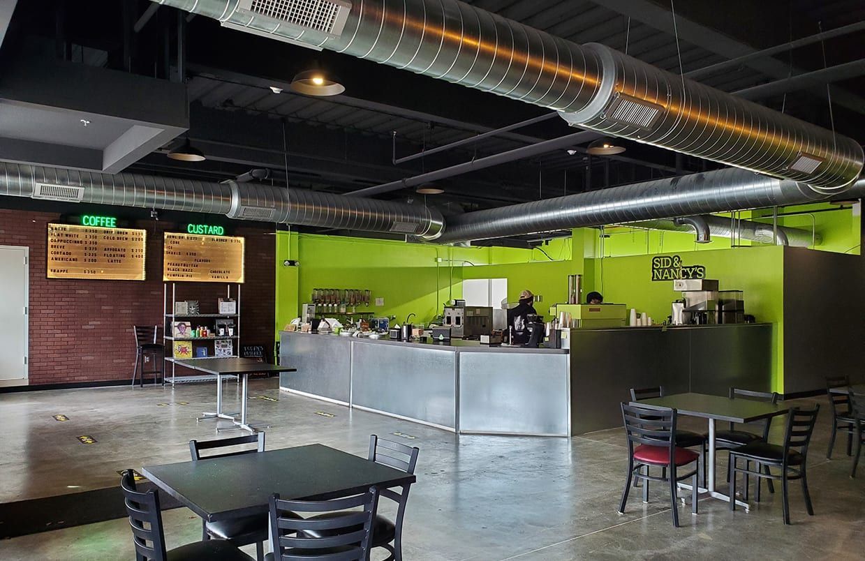 Empty modern café with green walls, metal counter, tables, and exposed ductwork.