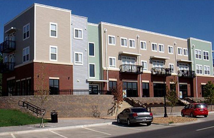 Modern apartment building with balconies, parked cars, and a brick retaining wall under a clear blue sky