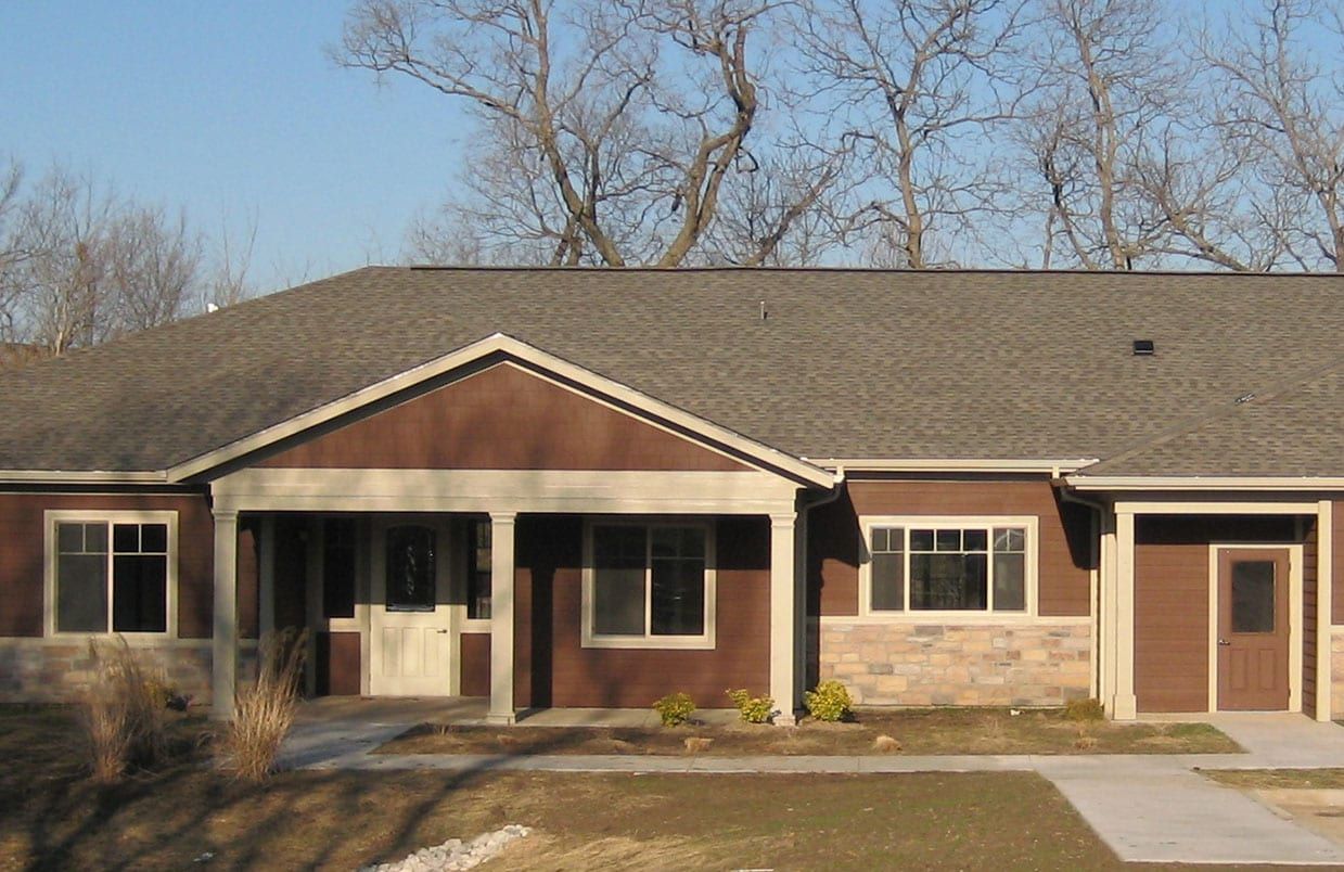Single-story brick building with a covered entrance, windows, and a brown door under a gray roof.