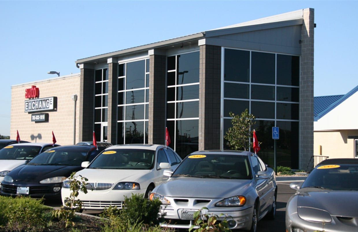 Cars parked outside a modern building with large glass windows and a blue roof.