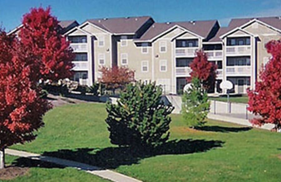 Apartment complex with green lawn and red-leaved trees under a clear blue sky