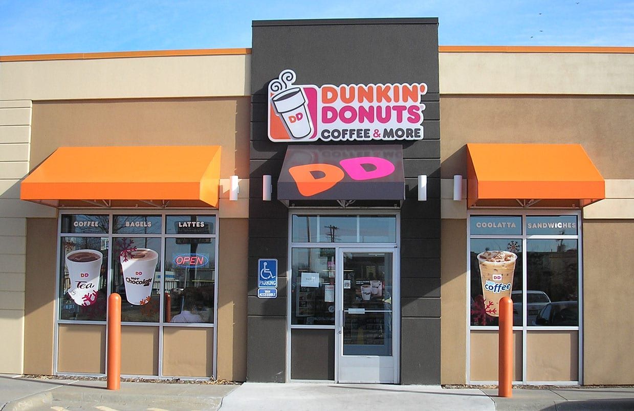 Dunkin’ Donuts storefront with orange awnings and glass doors on a sunny street.