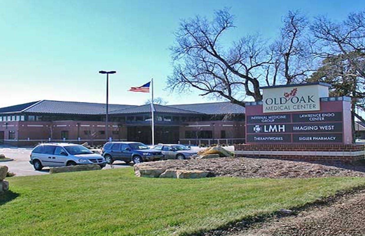 Brick school building with parked cars, an American flag, and a sign reading “Old Oak” in front.