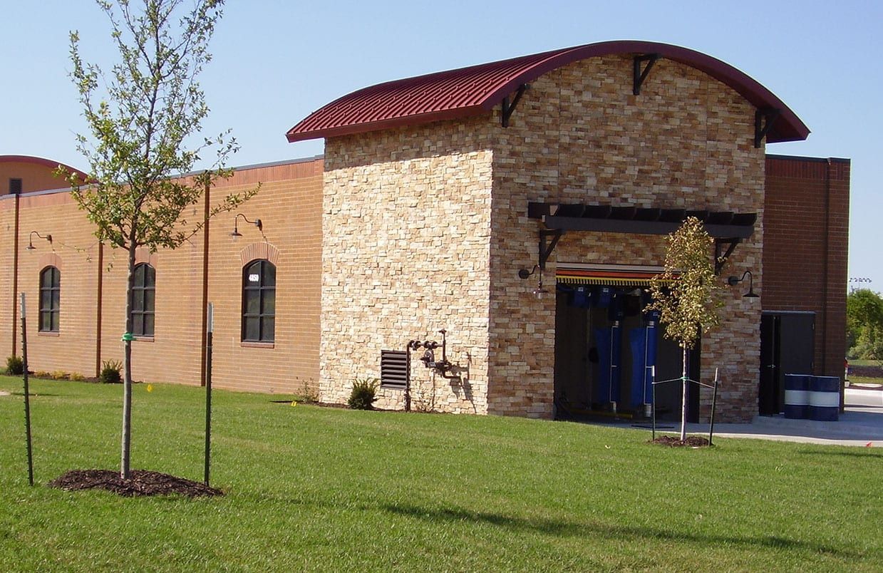Brick building with a curved red roof, arched windows, and a blue entrance on a grassy lawn