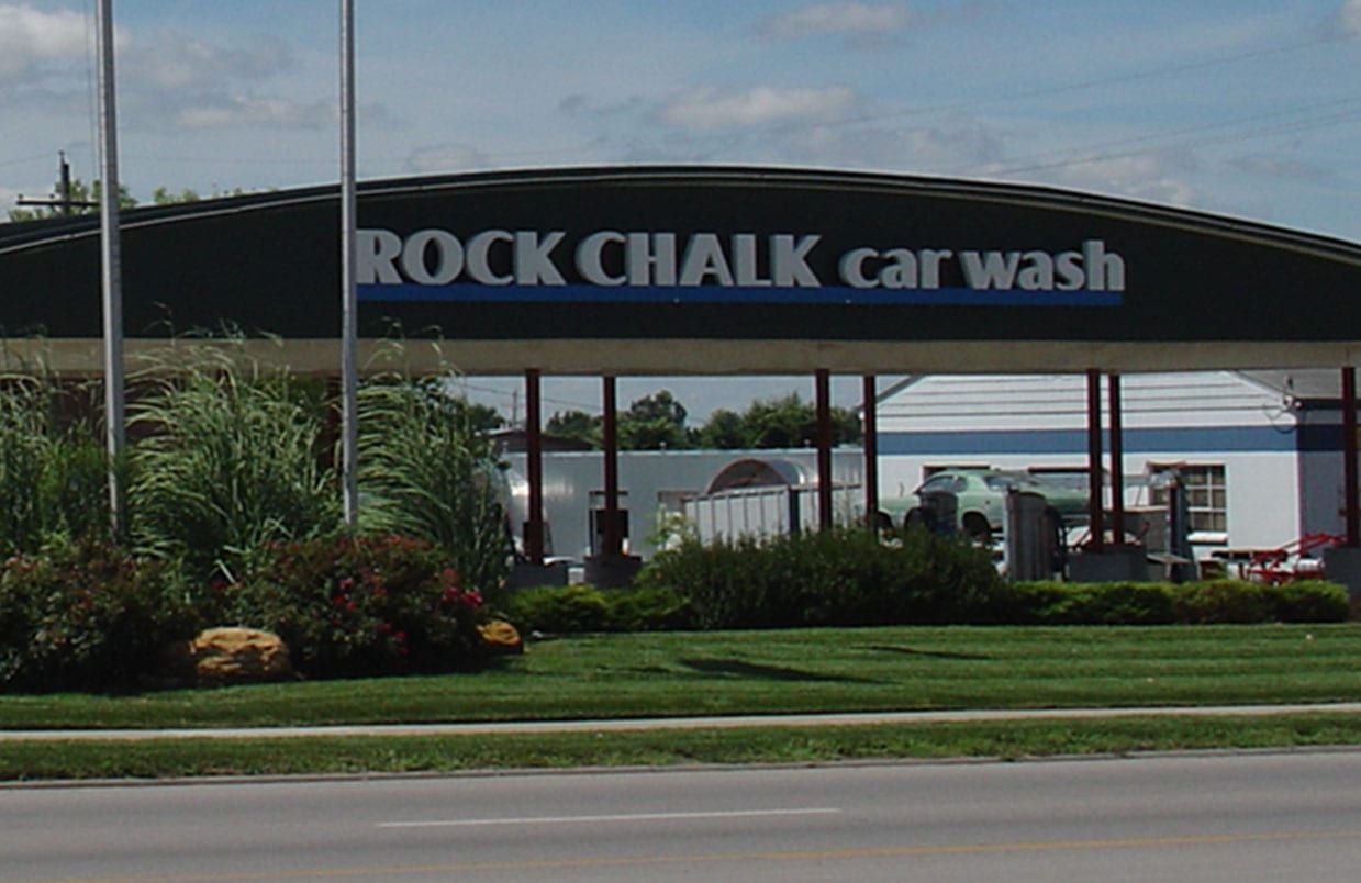 Rock Chalk car wash entrance with black arched sign, landscaping, and road in front