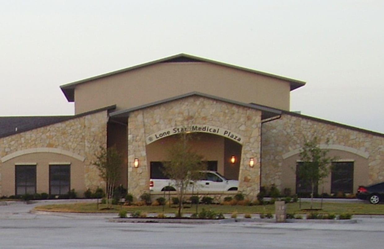 Front view of a beige church building with arched entryways and a car parked under the portico