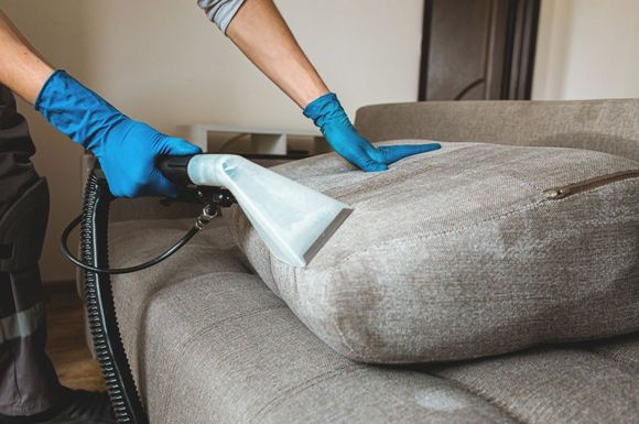 A person is cleaning a couch with a vacuum cleaner