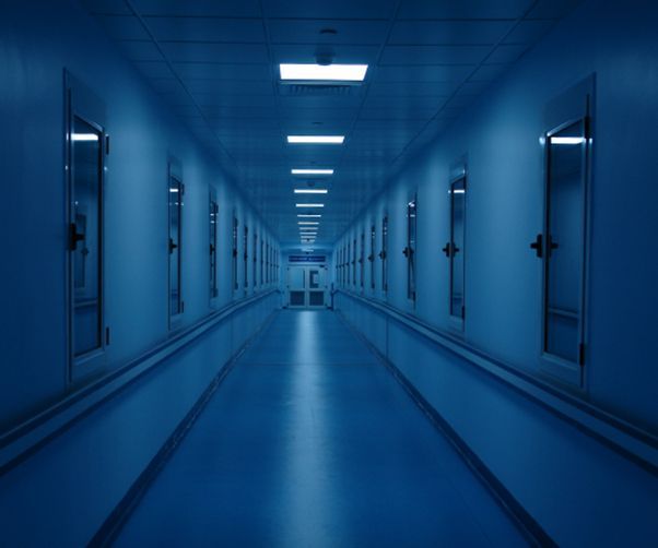 A long blue hallway with a lot of doors and lights on the ceiling.