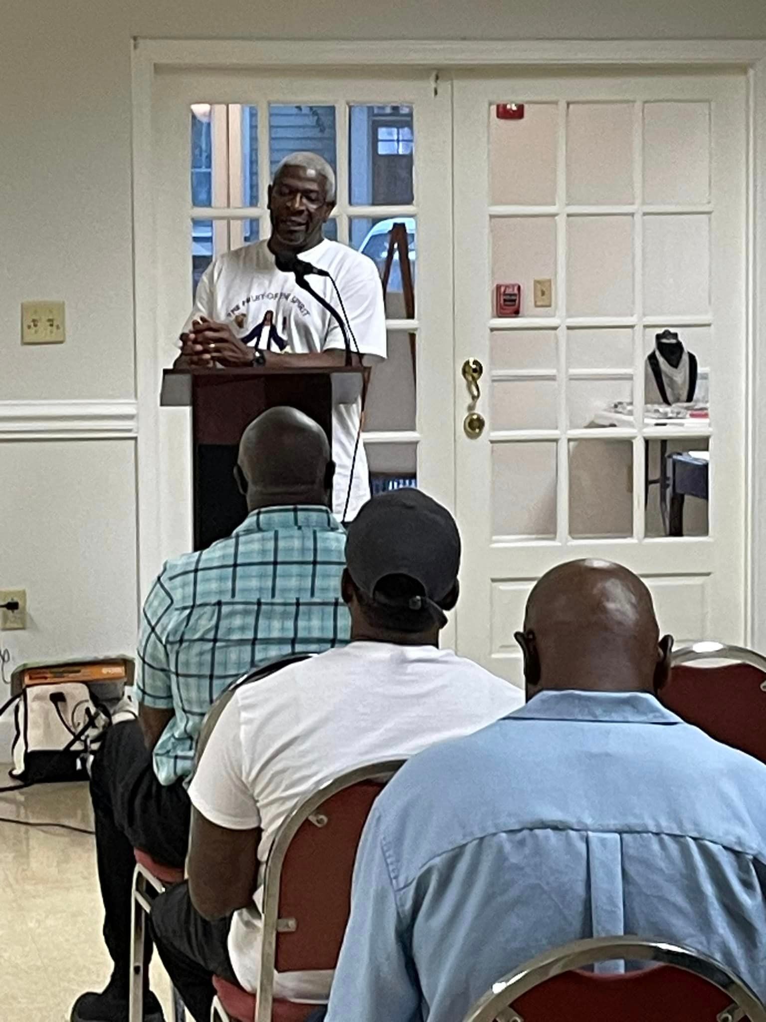 Man speaking from a podium to a seated audience indoors.