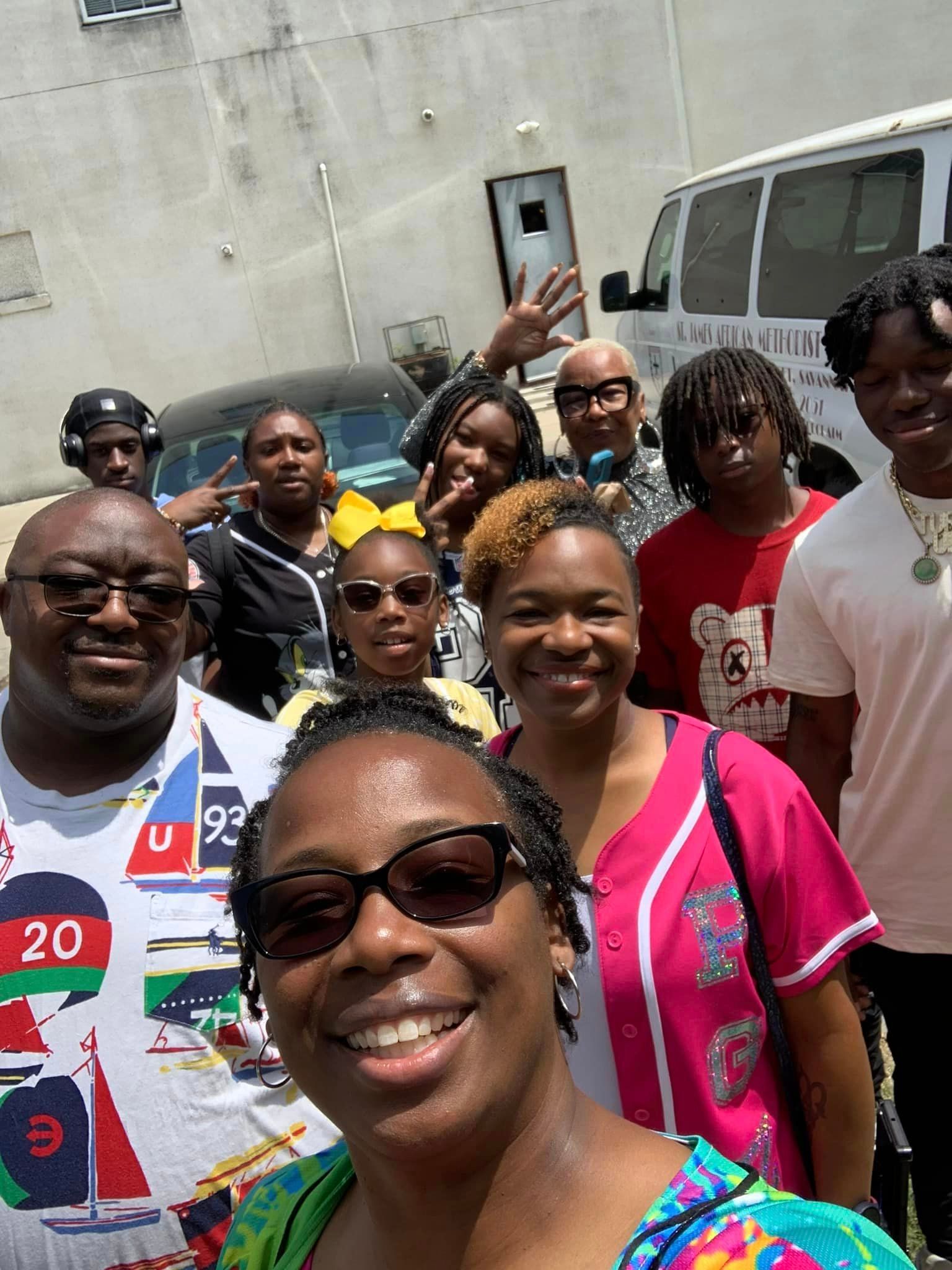 Group of people smiling outdoors near a van and building.