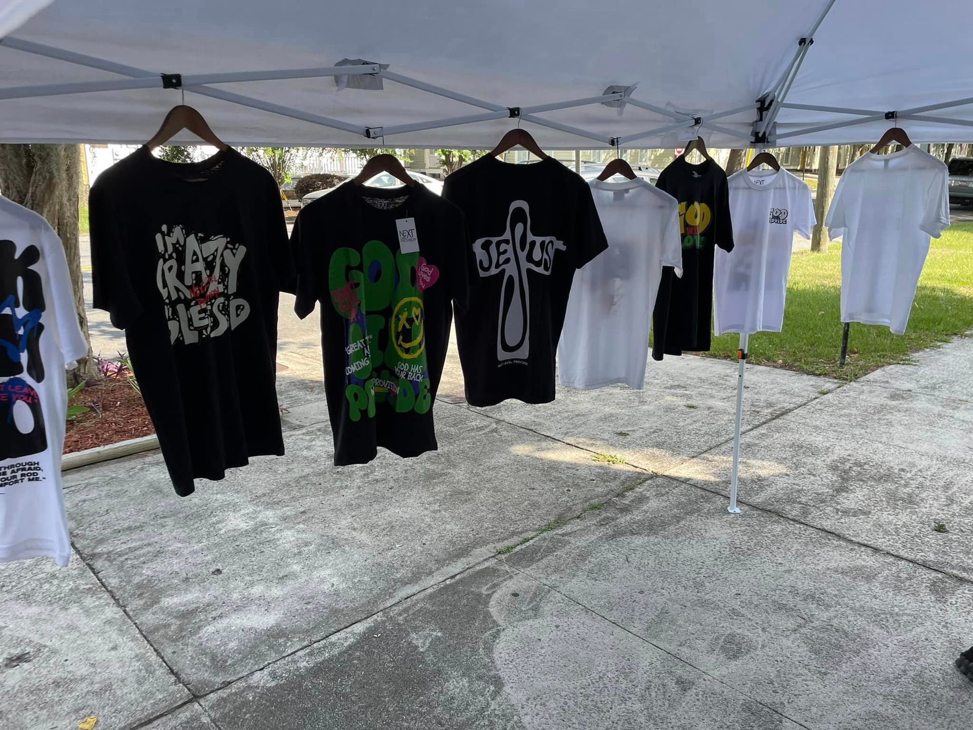 T-shirts hanging on display under a canopy, on hangers. Various designs and colors, outdoors.