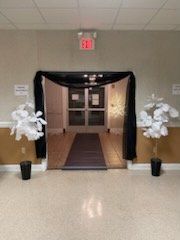 Entrance with black draping and white floral decorations, leading to a door with an exit sign.