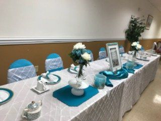 Table set for an event with teal and white decorations. Includes floral arrangements and place settings.