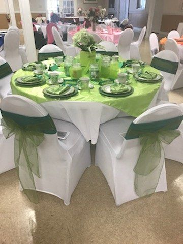 Round table set for a celebration, decorated in lime green. White chairs with green sashes surround the table.
