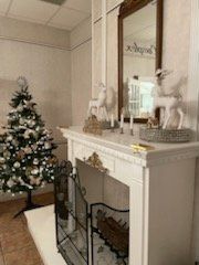 Christmas decor: tree, fireplace with reindeer statues, and a mirror in a light-toned room.