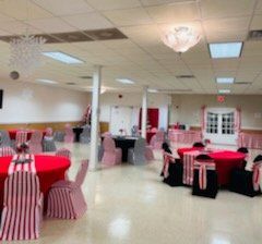 A large event room with red-clothed tables, striped chair covers, and white ceiling lights.