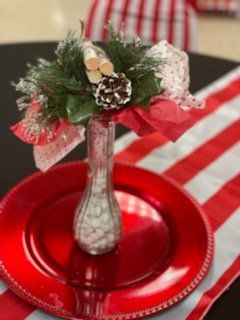 Red Christmas centerpiece: vase with greenery, pine cone, ribbon, on a red charger plate, striped runner.
