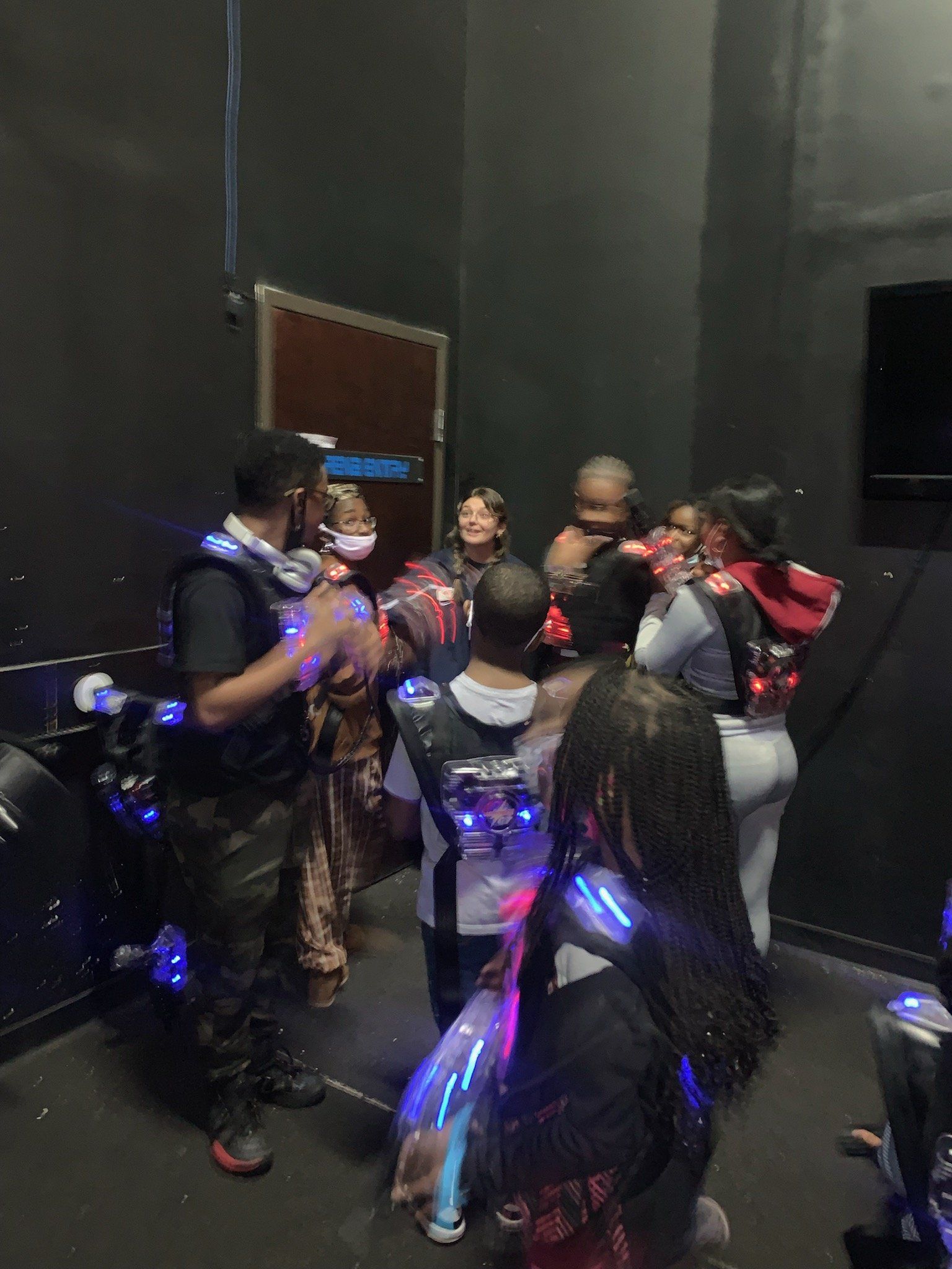 Group of people in laser tag gear, standing in a dimly lit arena, some smiling and holding equipment.