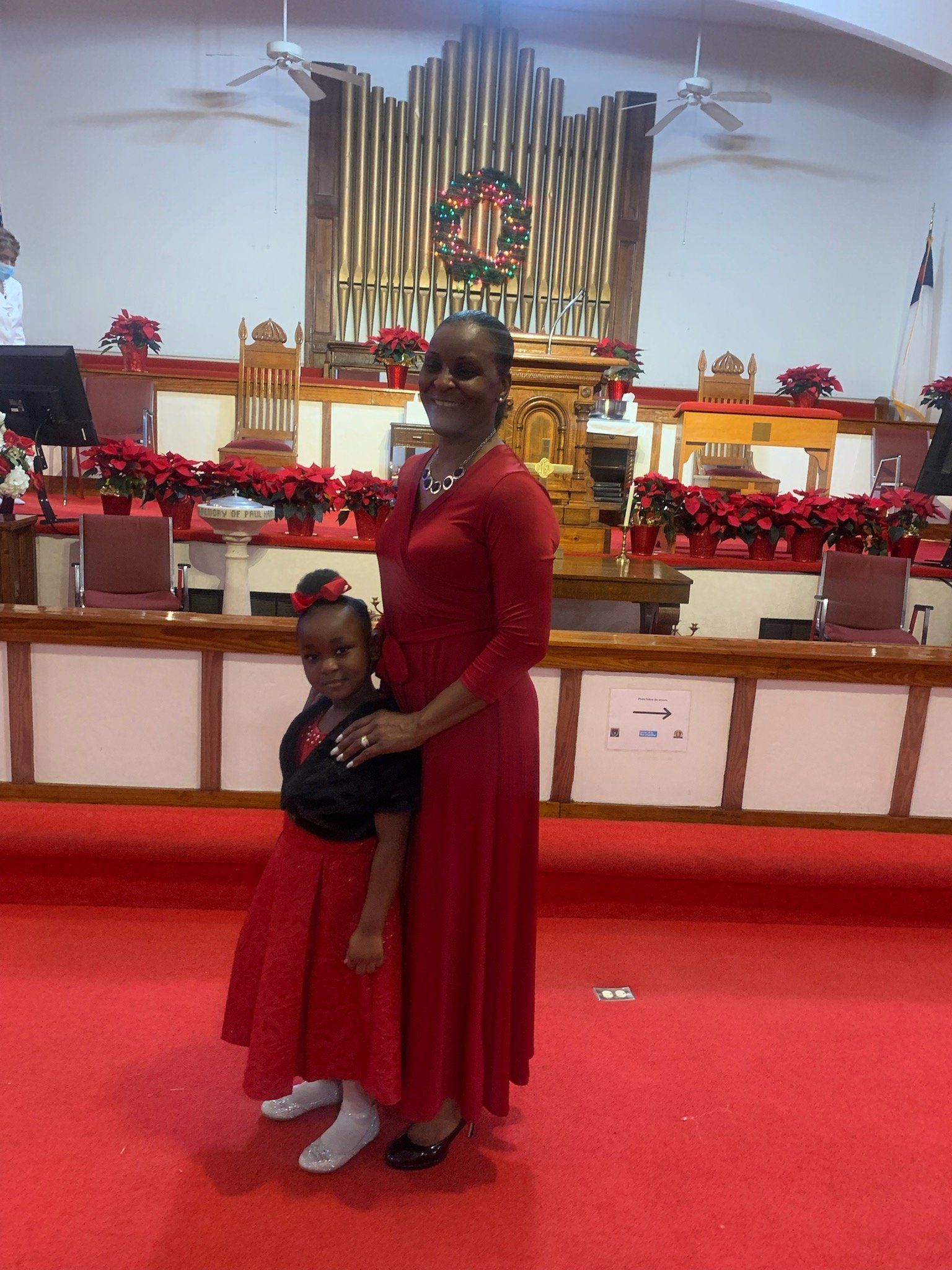 Woman and child in red attire stand on a red carpet in a church. A large pipe organ is in the background.