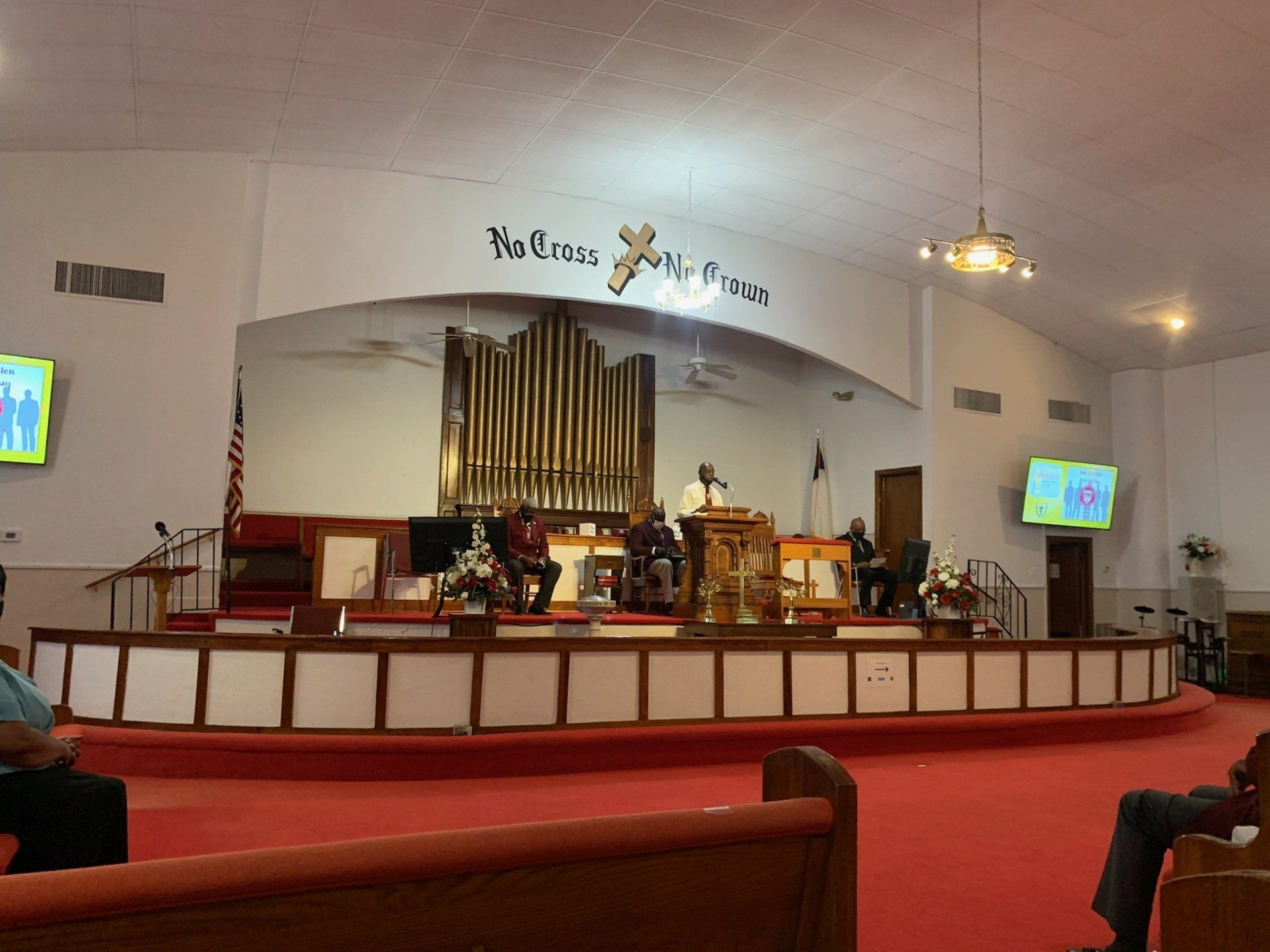 Interior church view: stage with organ, pulpit, choir, and seating. Red carpet, beige walls.