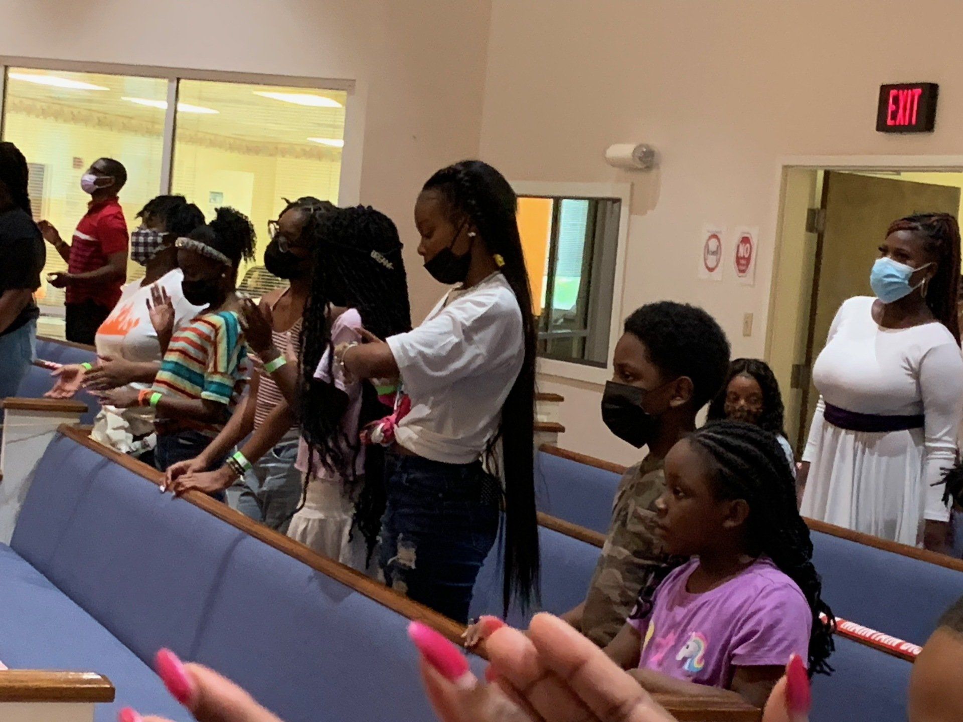 People praying in a church, some wearing masks, hands raised.