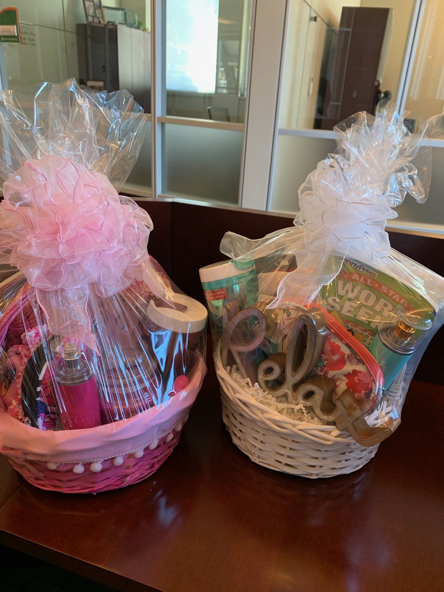 Two gift baskets wrapped in cellophane with pink and white bows on a dark table.