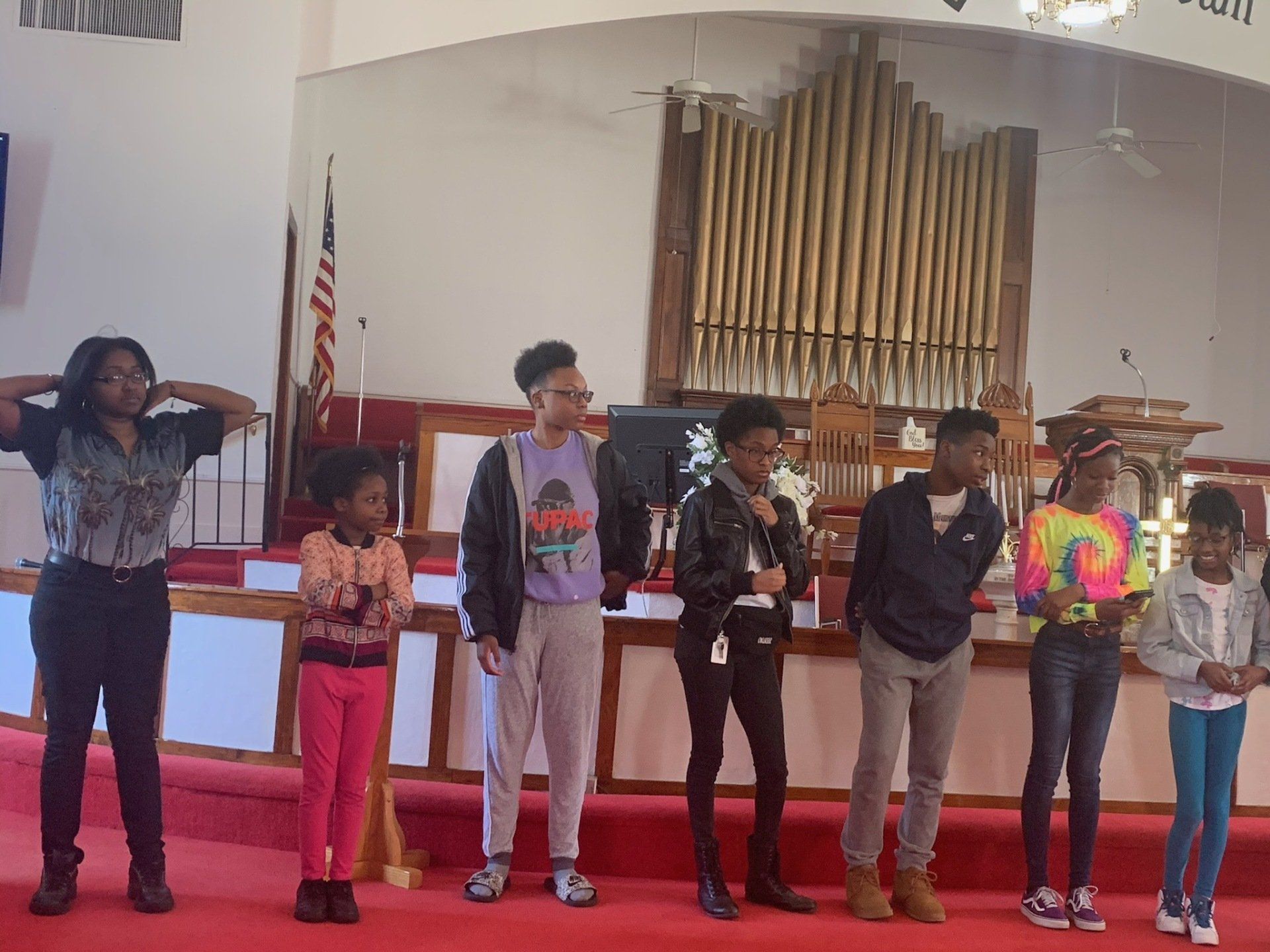Group of people standing on a red stage in a church. They are looking forward with various expressions.