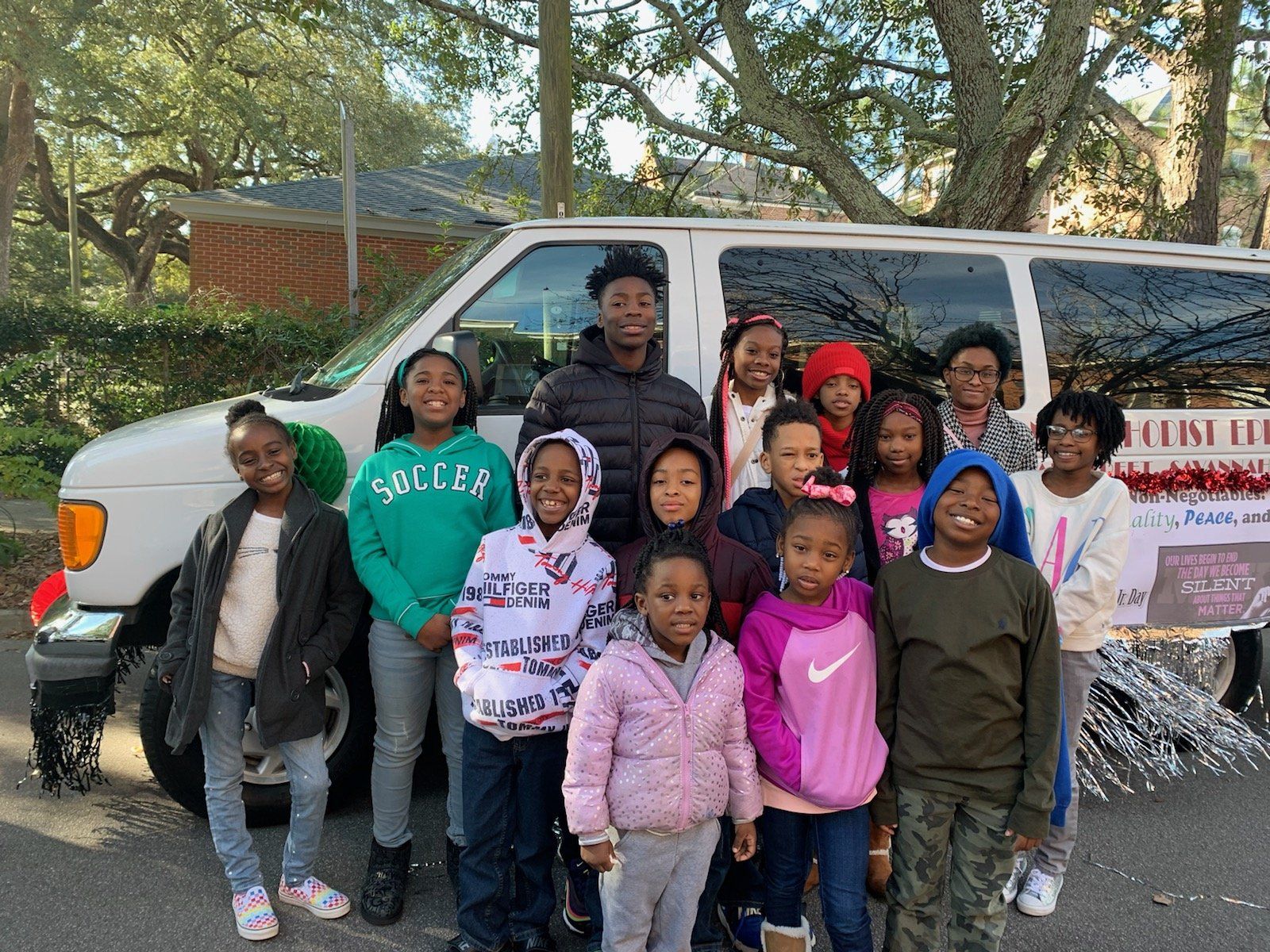 Group of children standing in front of a white van with decorations, outdoors.