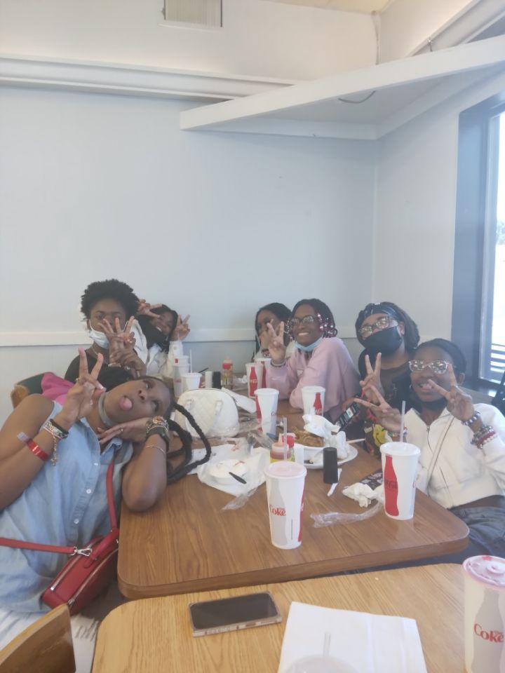 Group of people smiling, making peace signs, gathered around a table with drinks in a restaurant.
