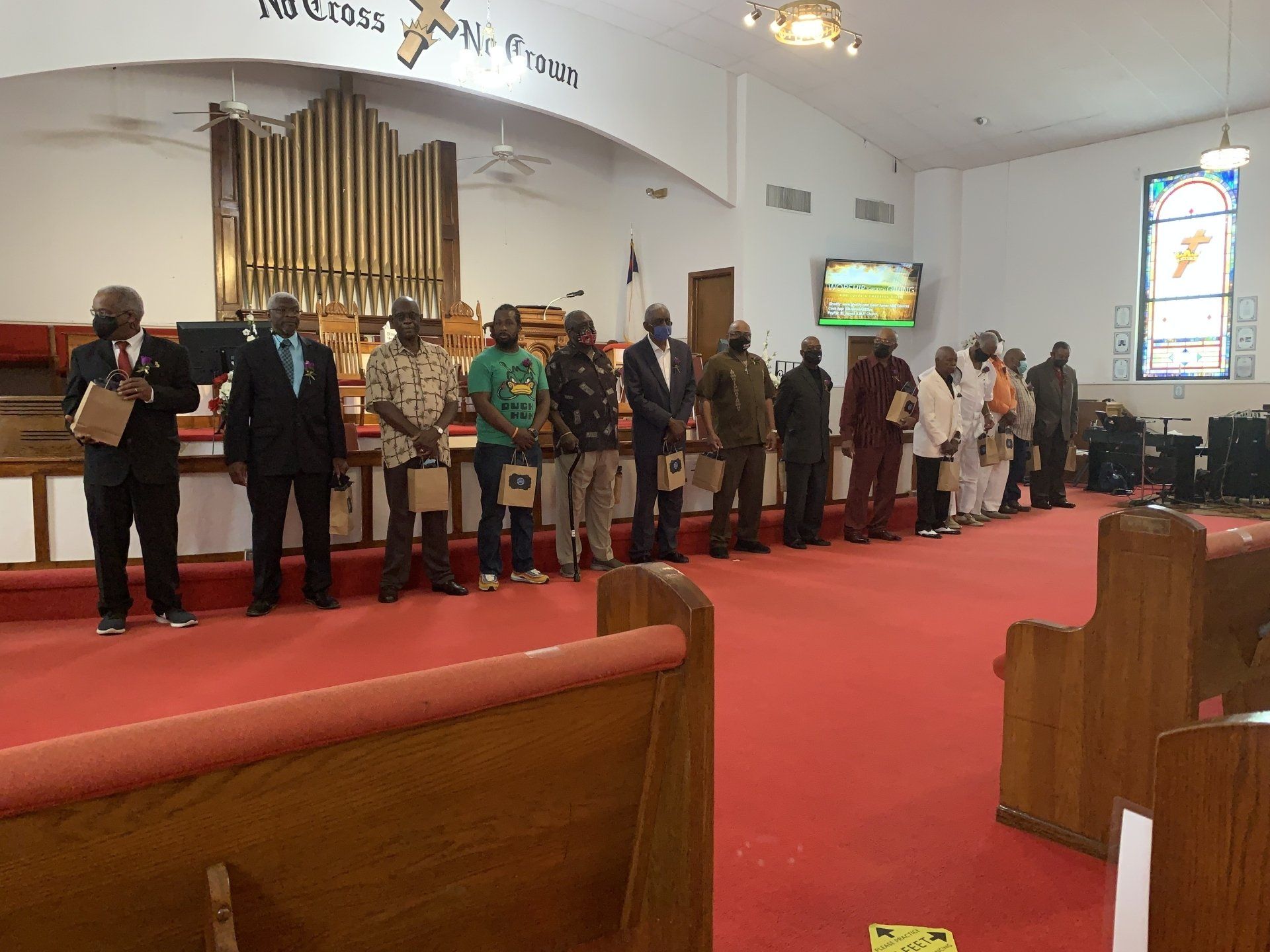 Men in a line in a church, some wearing sashes. Red carpet, pews, organ visible.
