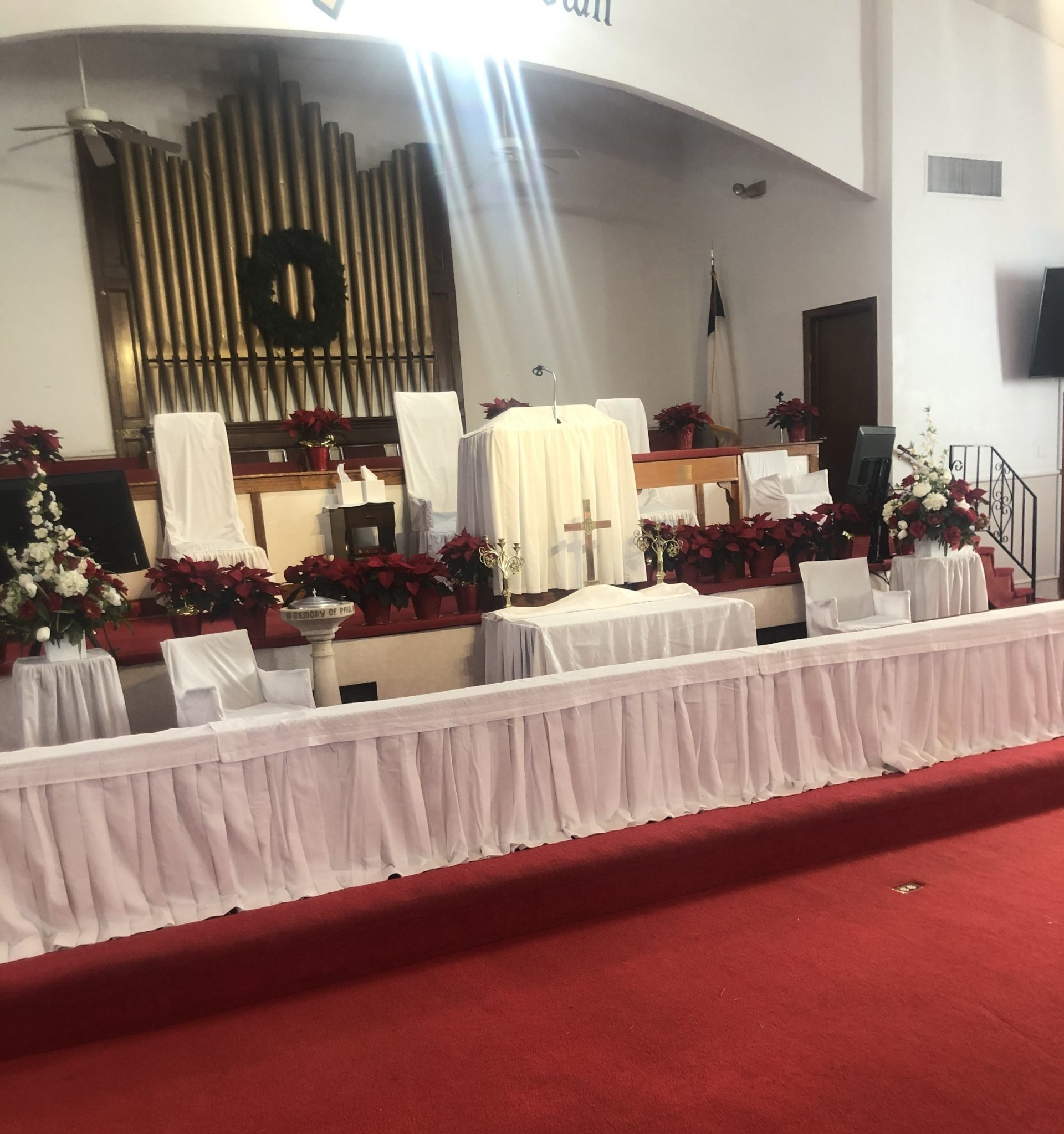 Church altar decorated with red flowers and white fabric, a large pipe organ in the background.