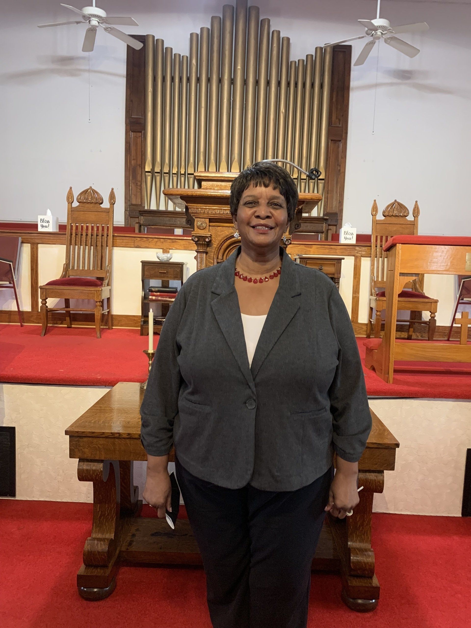 Woman in a blazer standing in front of a church altar with organ pipes.