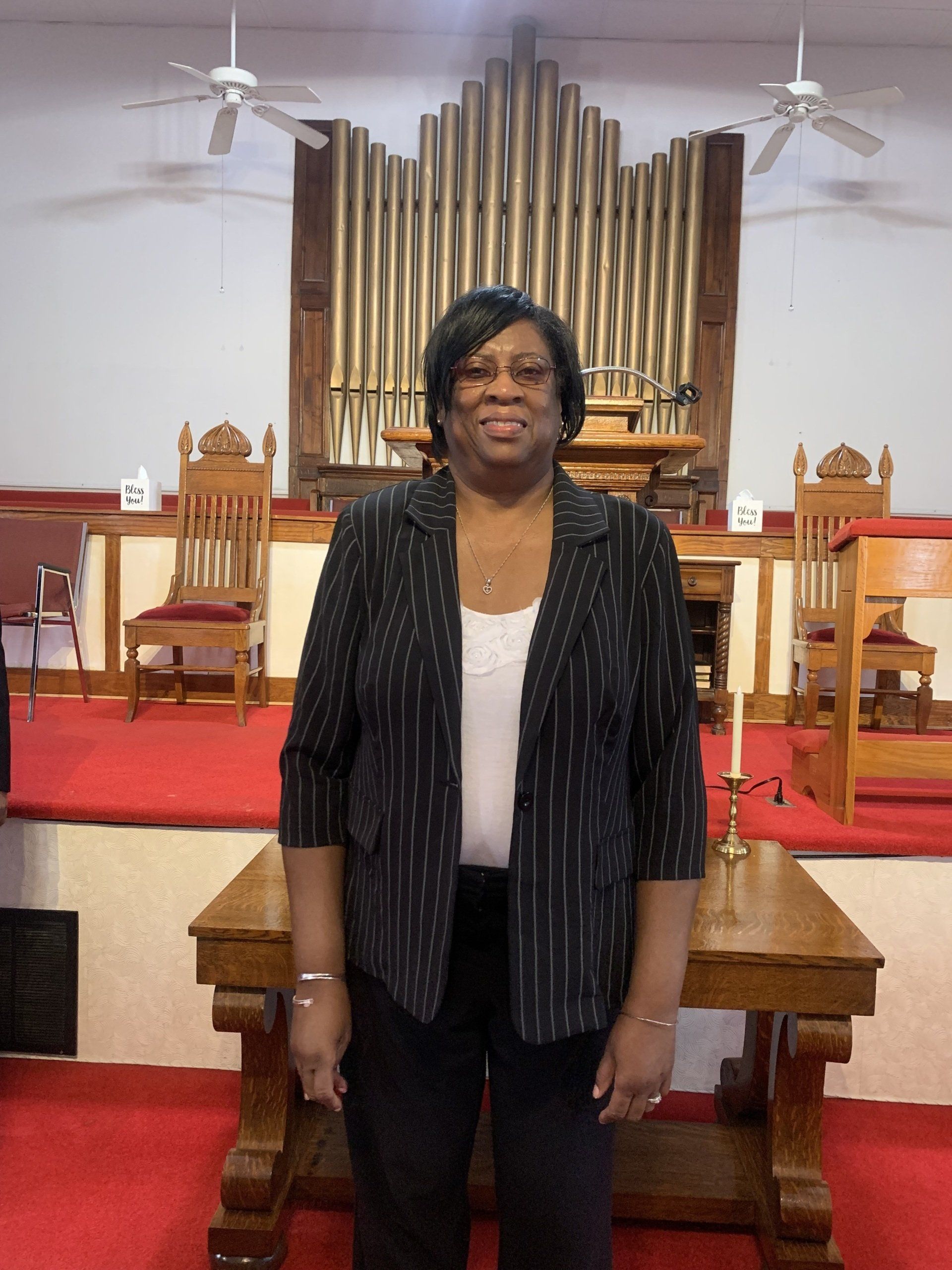 Woman in black blazer stands in a church, in front of a pipe organ.