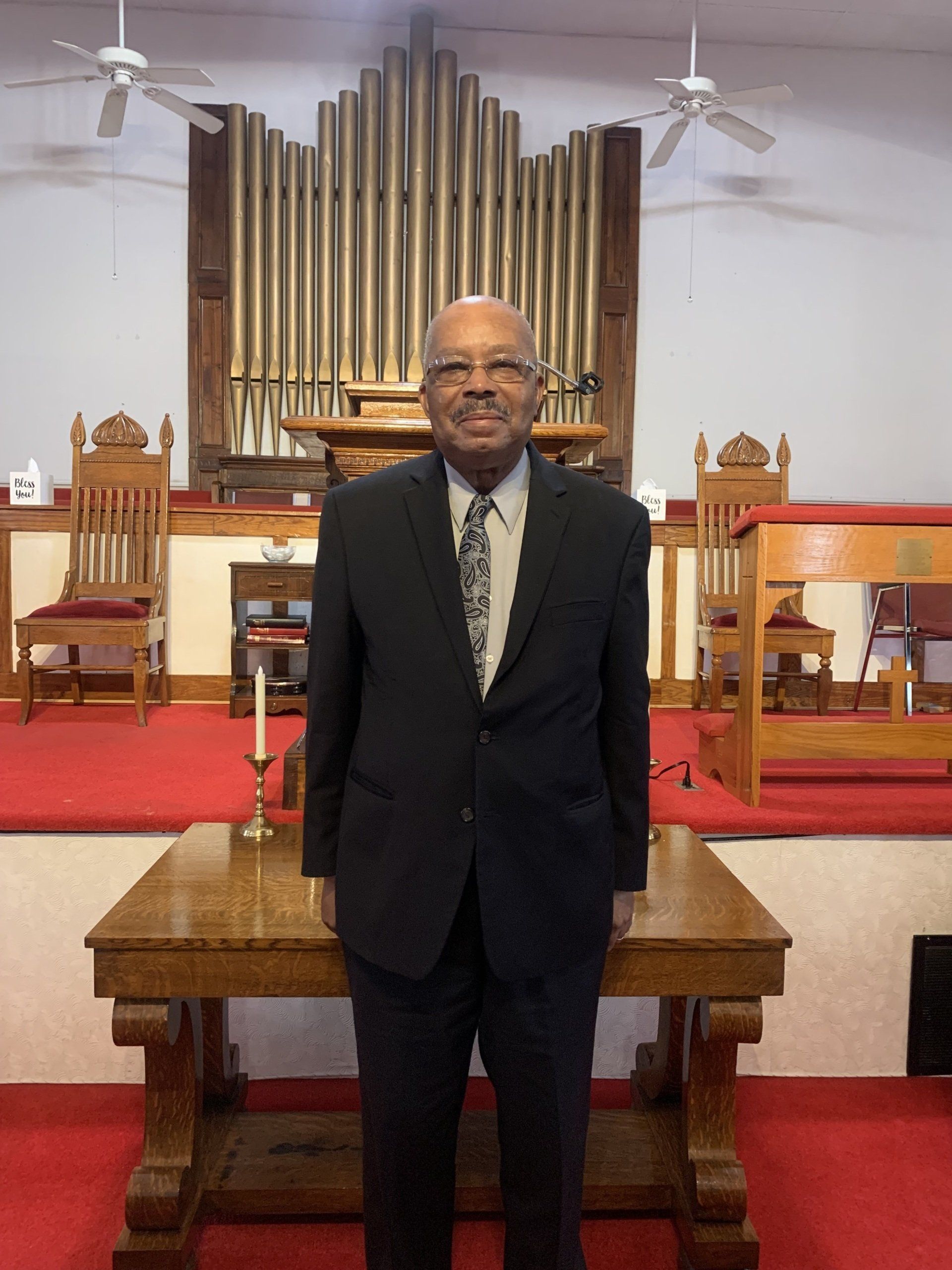 Man in suit stands in front of a church altar with an organ in the background.