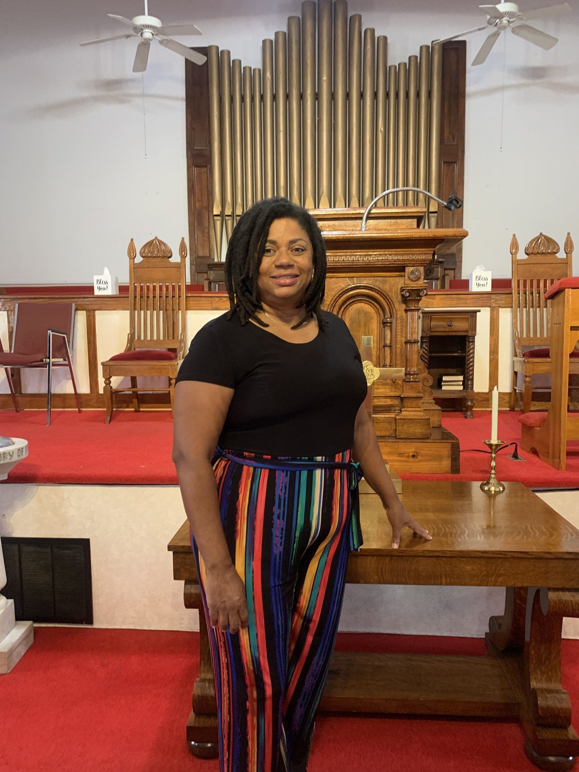 Woman in colorful pants stands in front of a church altar with a pipe organ in the background.