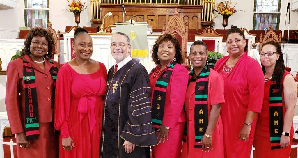 Group of people in red outfits and sashes with a clergyman in a church.