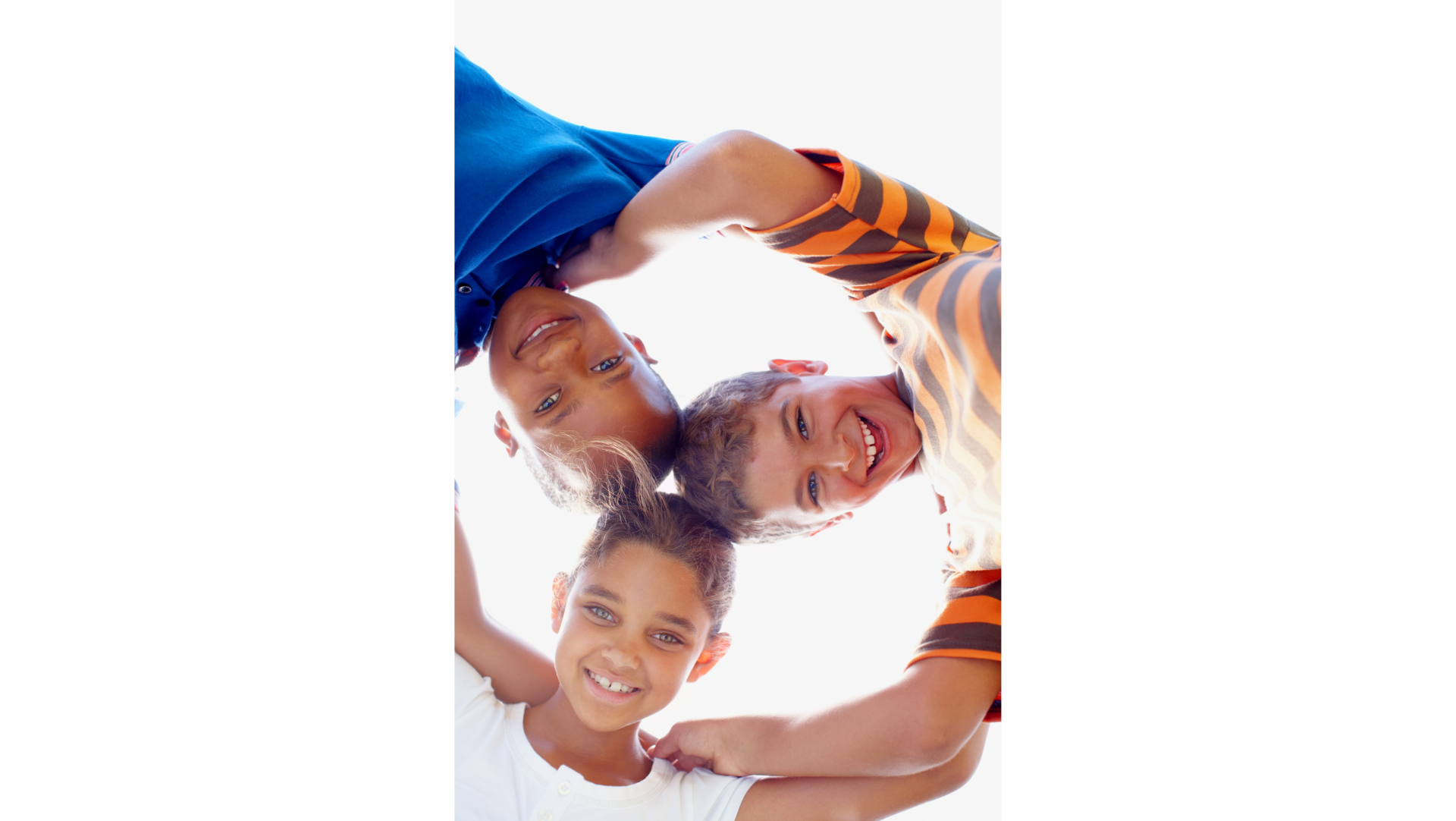 Three children smiling, heads together, forming a circle. Viewed from below, bright background.