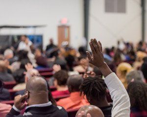 Audience with raised hand in an auditorium. People seated, some facing the front.