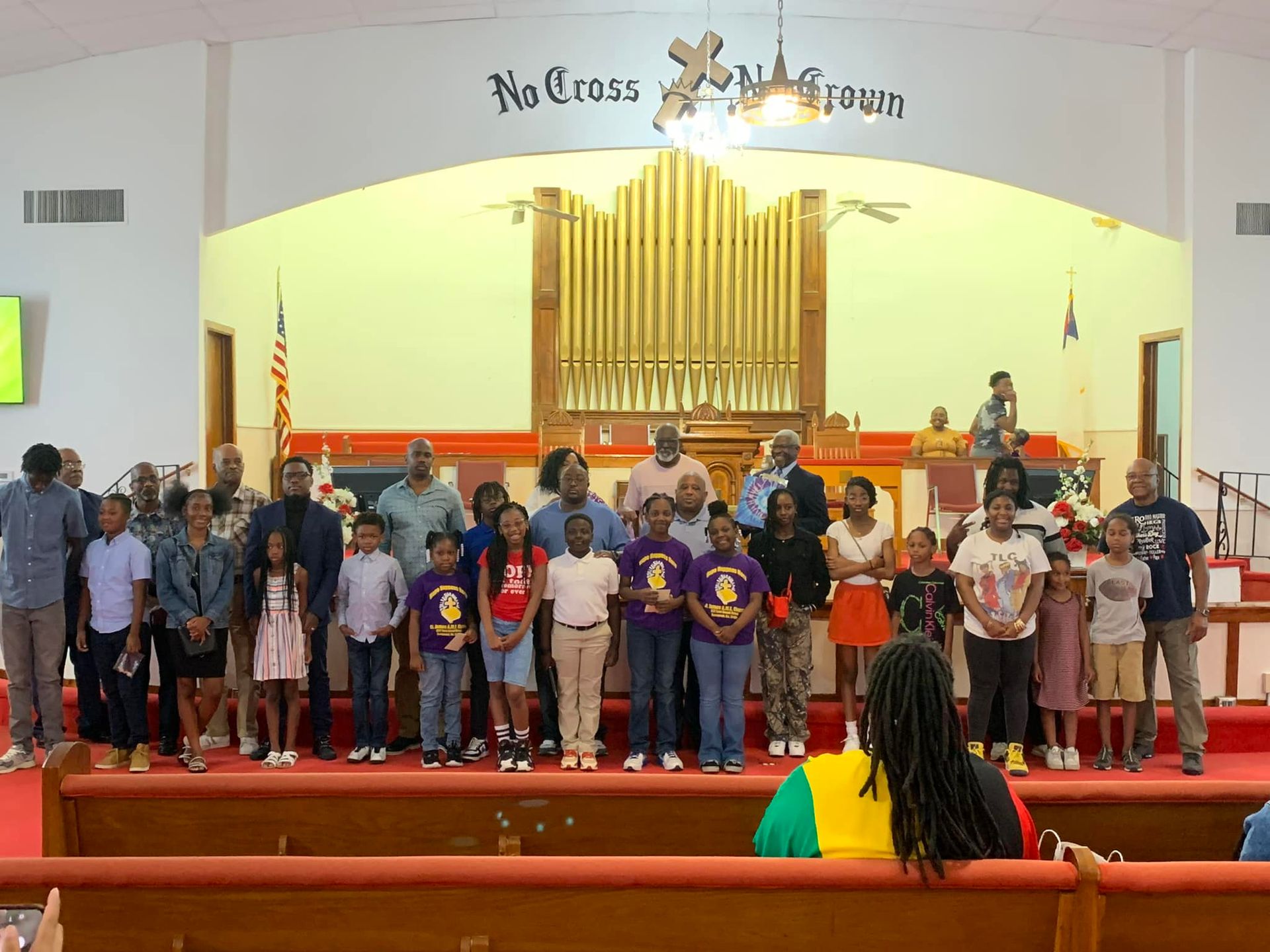 Group of people standing on a church stage, with a large organ in the background.