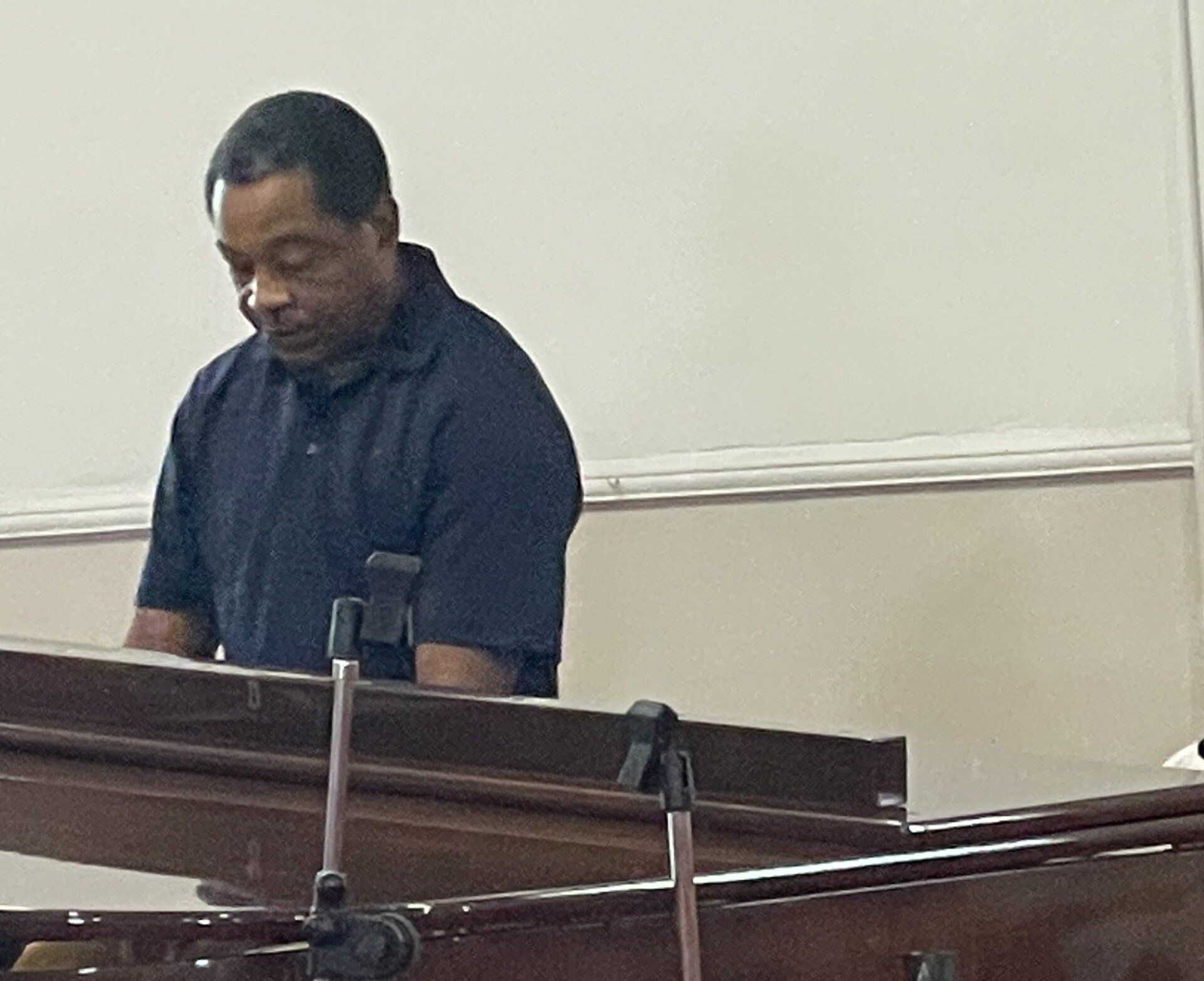A person playing a keyboard; they are seated in front of it and looking down. The background is white.