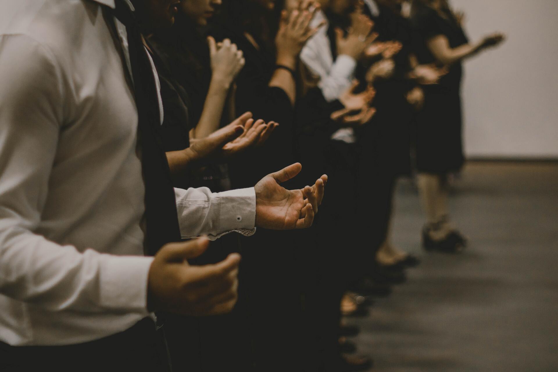 People in formal attire with hands extended, possibly praying or receiving something.