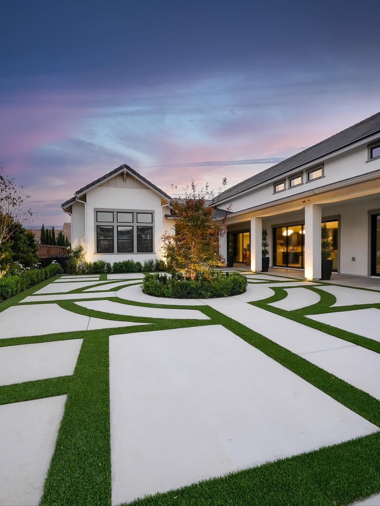 Modern home courtyard with white stone paving, green grass lines, and warm lights at dusk