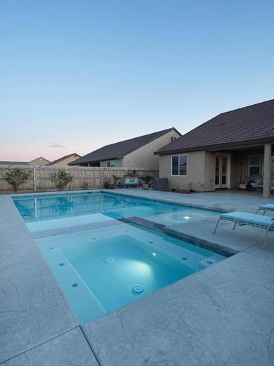 Modern backyard pool with spa and patio beside a house at dusk