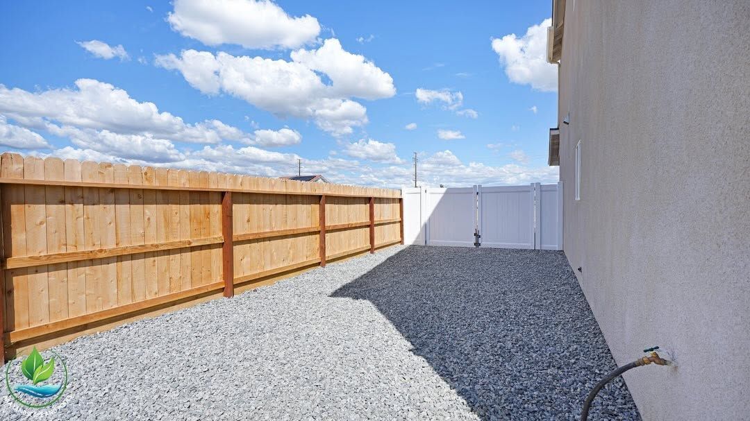 Gravel backyard with wooden fence, white house wall, and blue sky with clouds